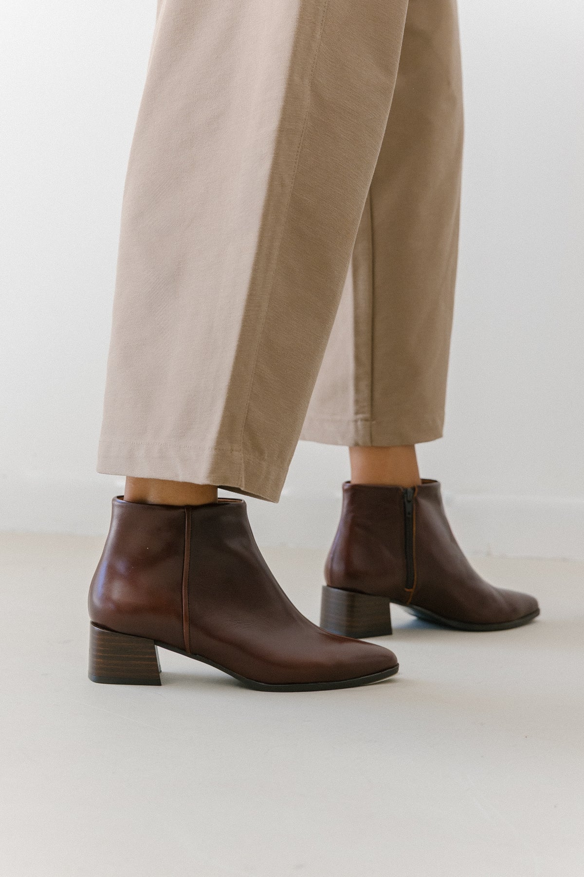 Botins bordeaux em pele em passo, com calças claras pelo tornozelo.