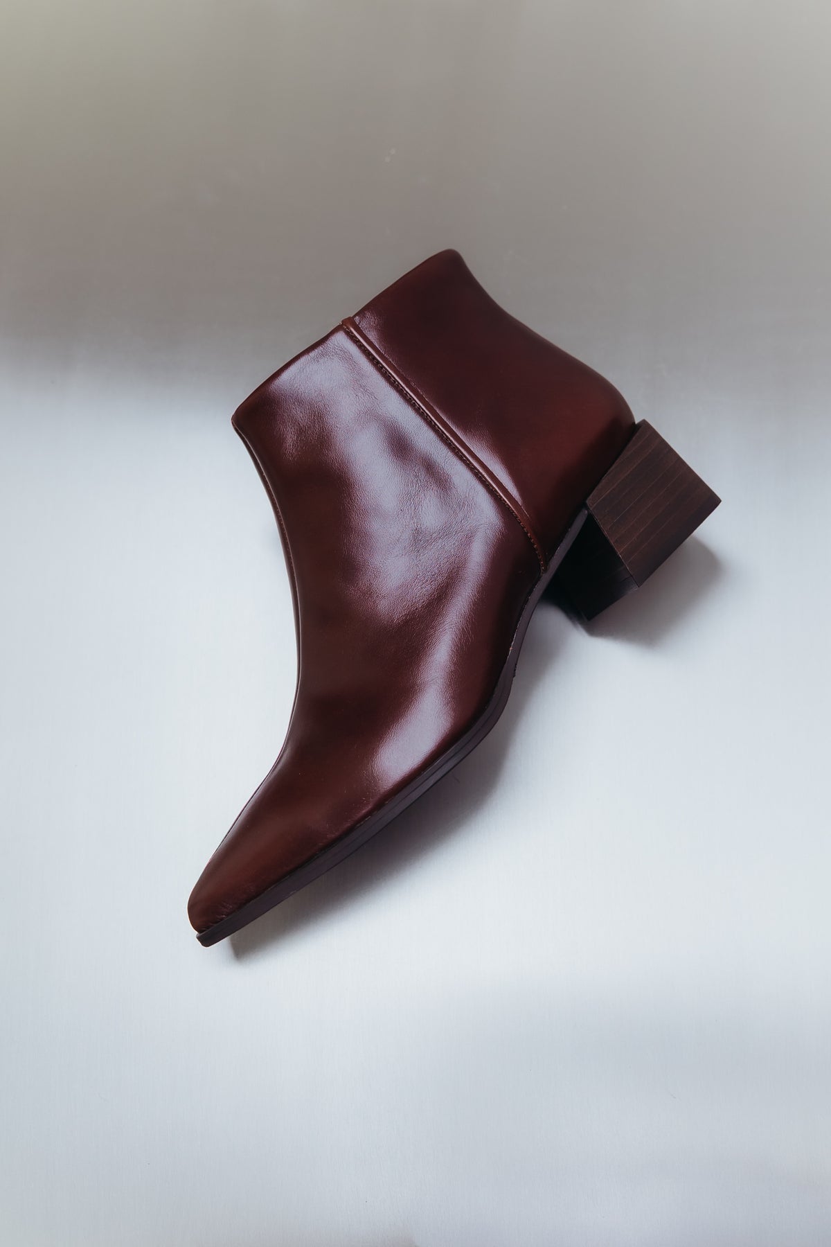 Botins bordeaux numa imagem de campanha, com casaco de camurça castanho e fundo vermelho.
