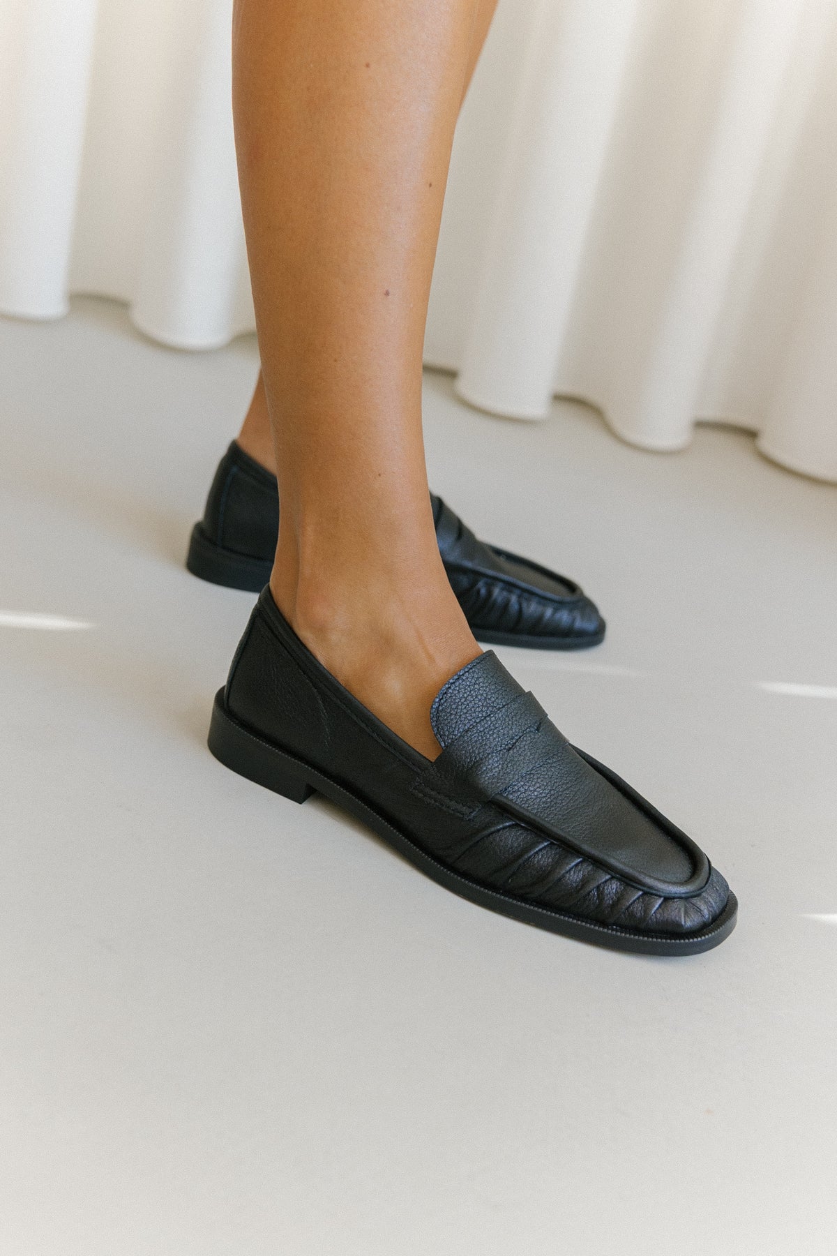 Mocassins pretos da Zilian em pele soft, com salto de bloco, usados com saia branca.