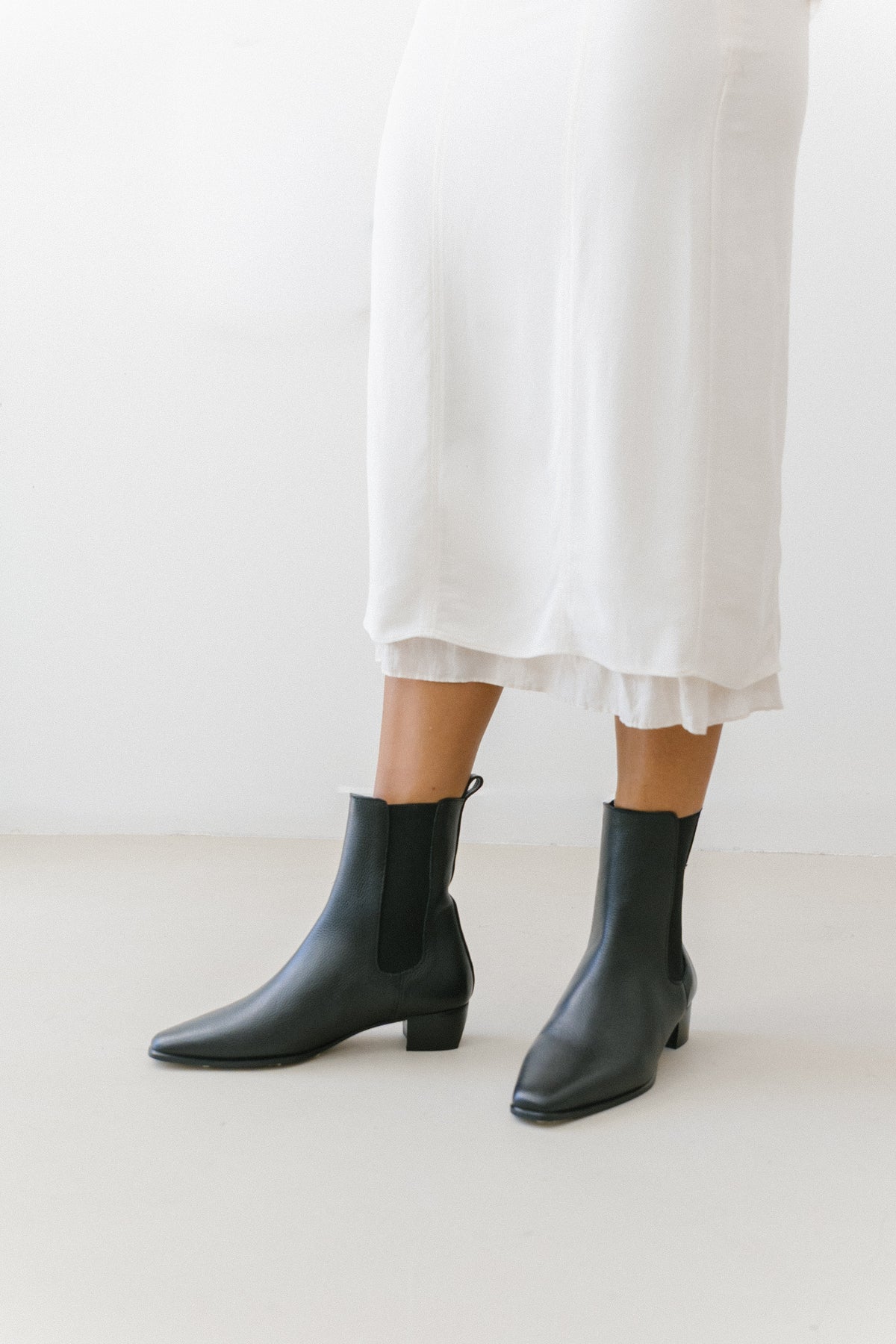 Botas pretas com elásticos laterais da Zilian, usadas com saia branca comprida.
