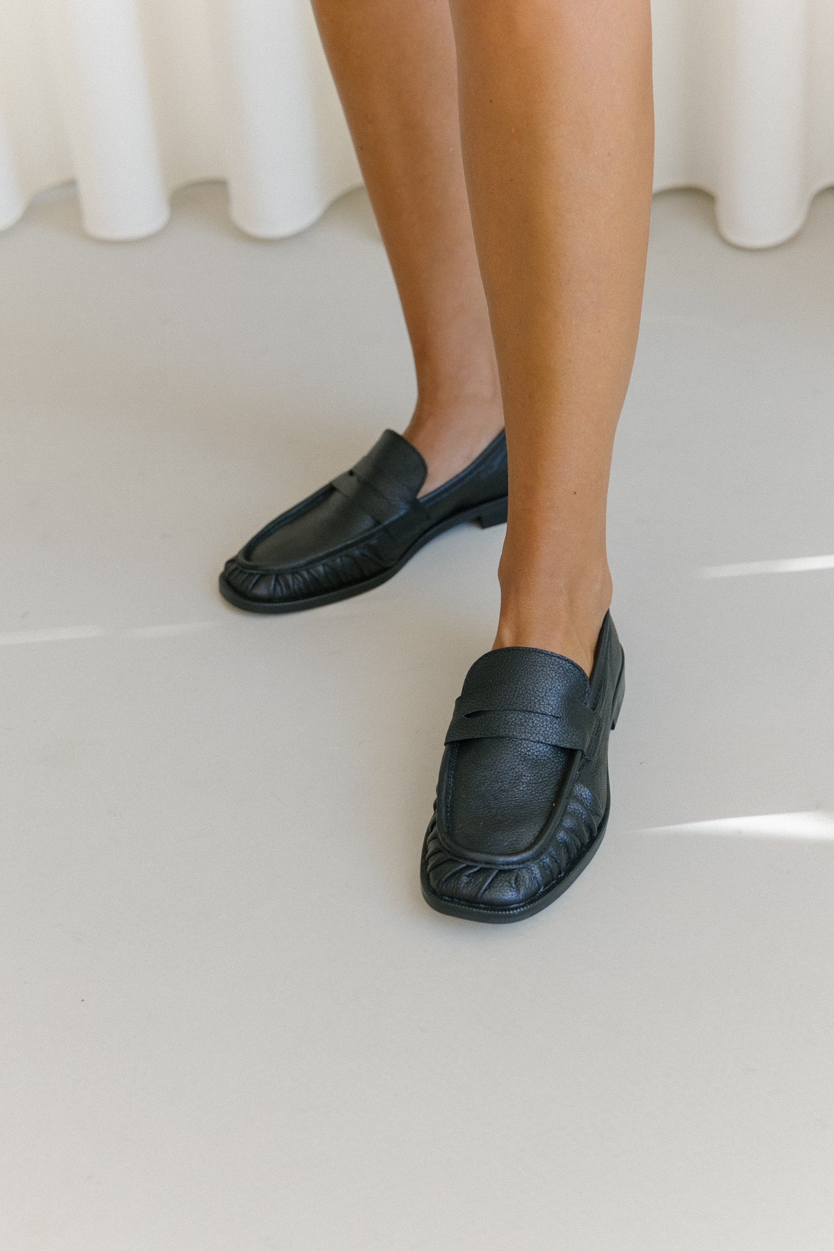 Loafers em pele soft preta texturada, com travessão à frente e biqueira franzida.