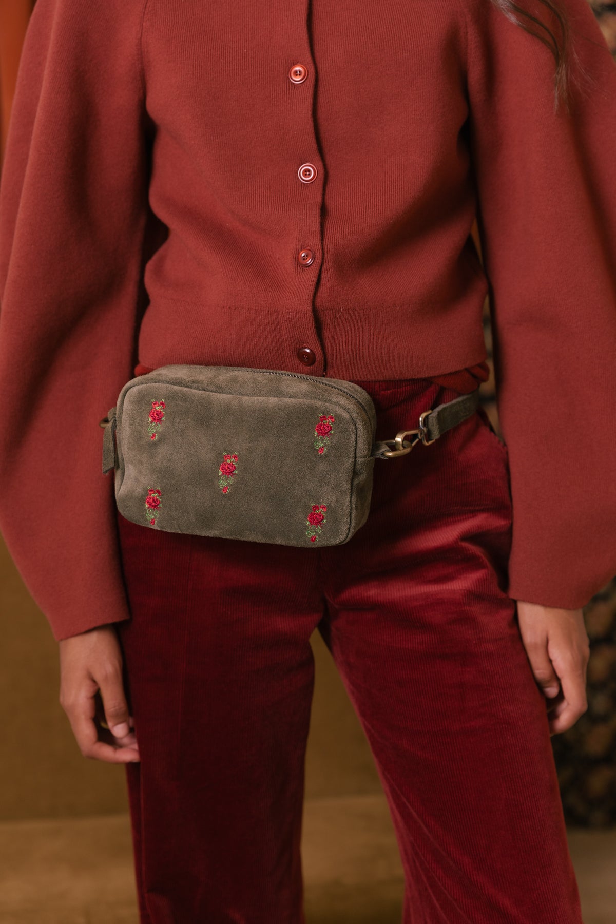 Bolsa em croute verde com rosas bordadas, levada à cintura sobre calças de bombazina bordeaux